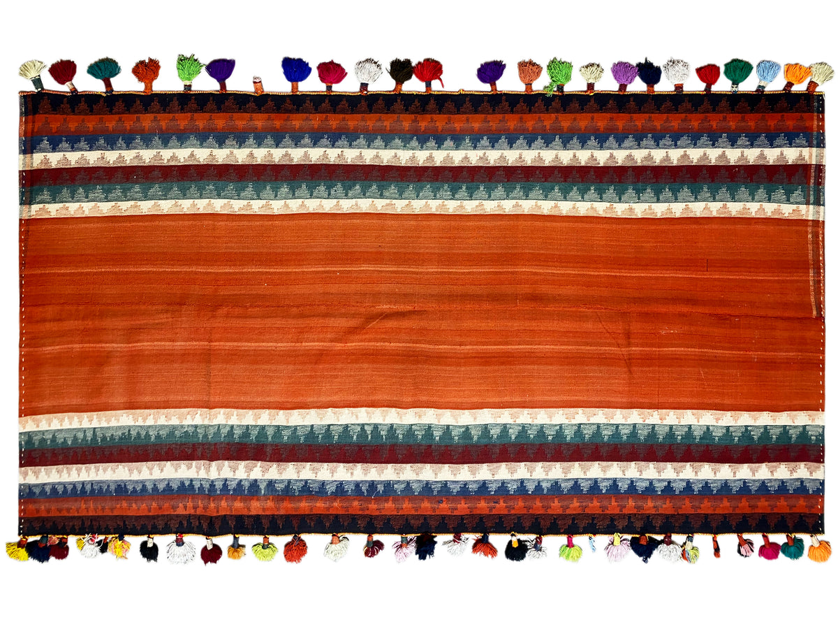 Vista dettagliata del tappeto Jajim: ampia fascia in terracotta con bordo e vivace frangia multicolore