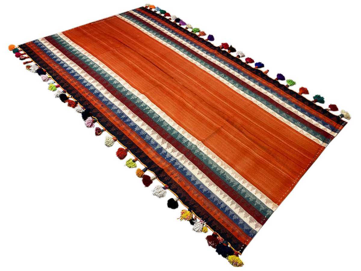 Tappeto Jajim disposto in diagonale: terracotta, bordo a righe, nappe in diversi colori