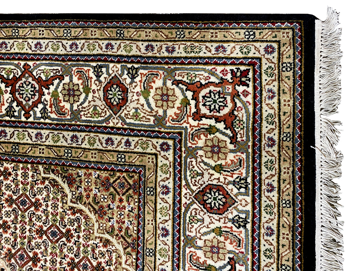 Dettaglio del bordo di un tappeto Indo-Tabriz marrone con ornamenti variopinti e frange a destra