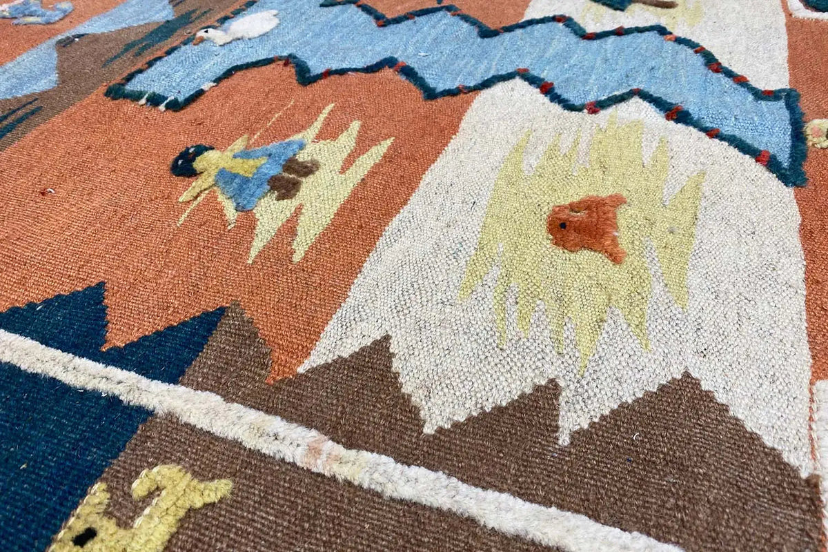 Dettaglio di tappeto kilim con motivi floreali e a zigzag in marrone, blu e crema
