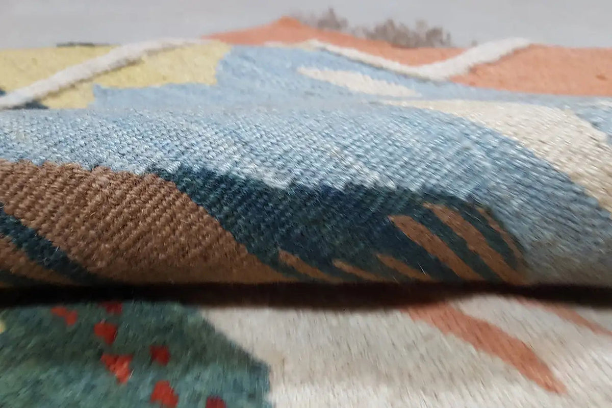 Primo piano di un tappeto kilim: superficie tessuta con motivo blu-marrone e struttura goffrata