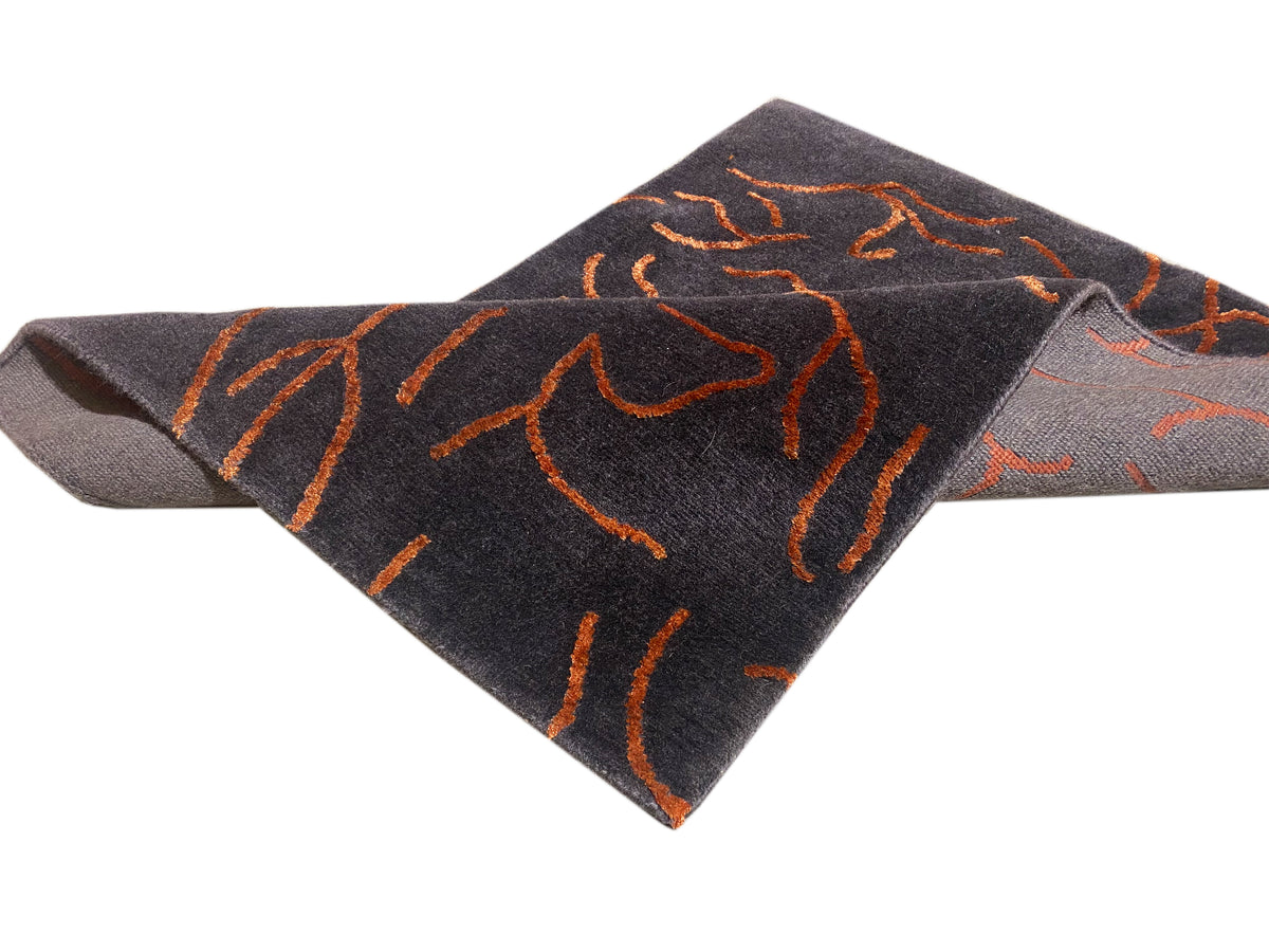 Tappeto di design grigio scuro con motivo astratto arancione, vista con effetto piegato