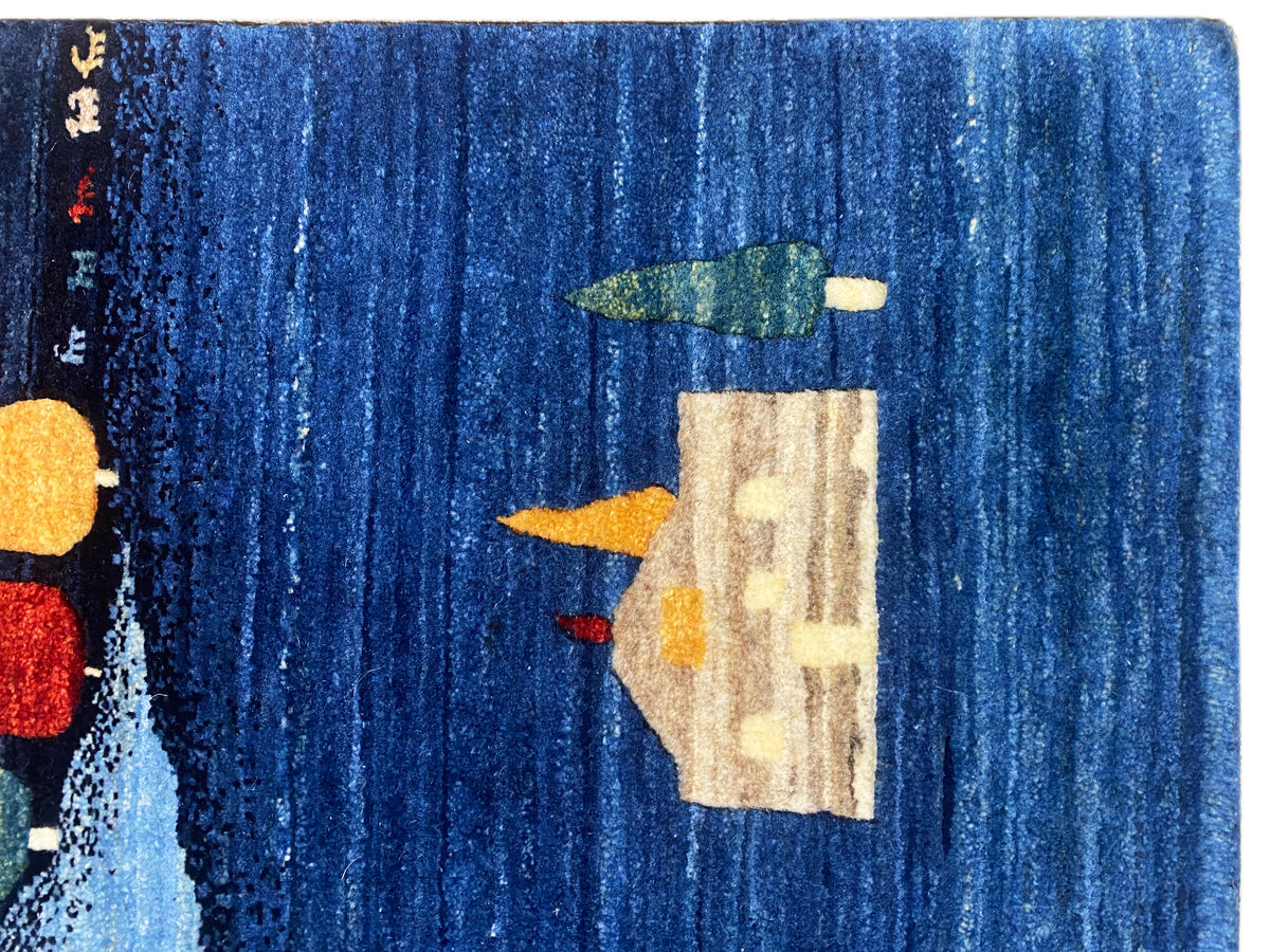 Gabbeh-Luri Teppich Detailansicht: blaue Fläche mit beigem Hausmotiv und bunten Bäumen.