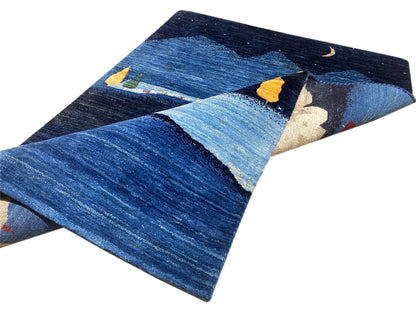 Gabbeh-Luri Teppich mit diagonaler Ansicht: Blau mit Berglandschaft und beigen Hausformen.