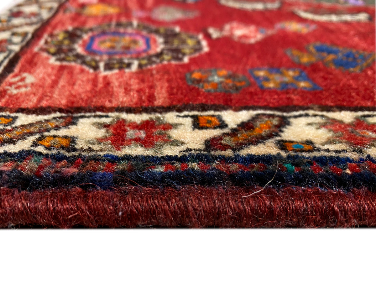 Dettaglio del tappeto Poshti 58x57 cm: pelo rosso, bordo con motivi colorati e corte frange