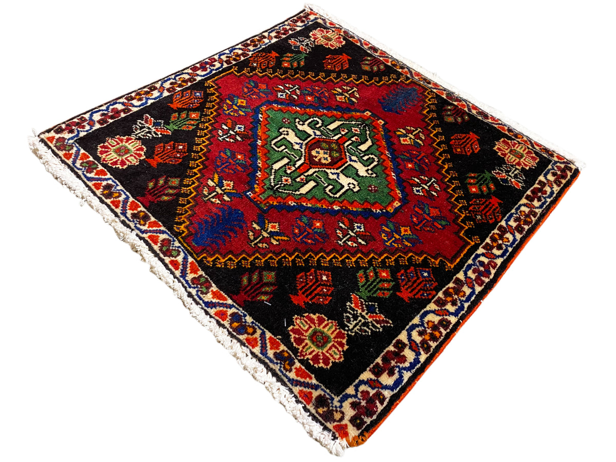 Tappeto Poshti 56x56 cm, quadrato, con bordo rosso e piccoli dettagli colorati su fondo nero