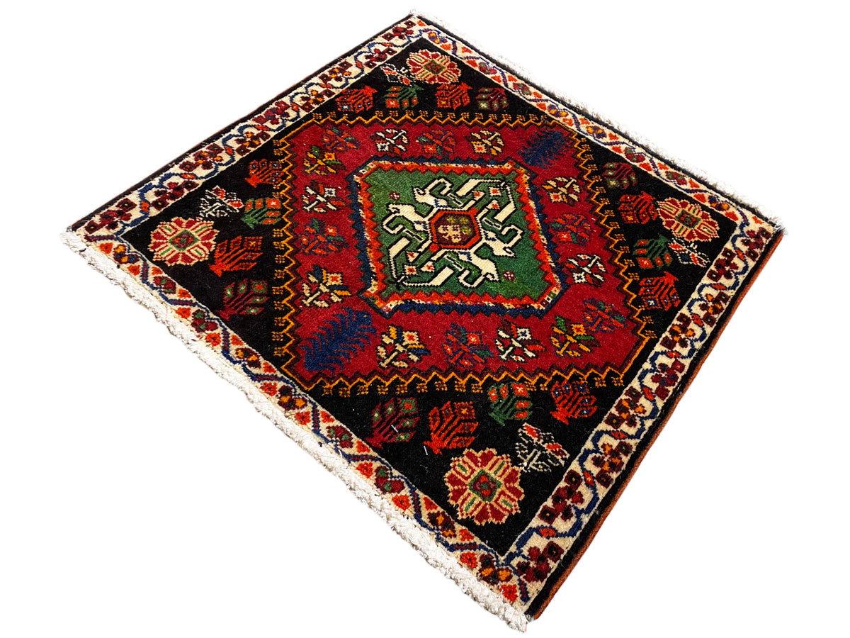 Tappeto Poshti quadrato, in diagonale: tappeto tessuto nero con motivo centrale verde-rosso