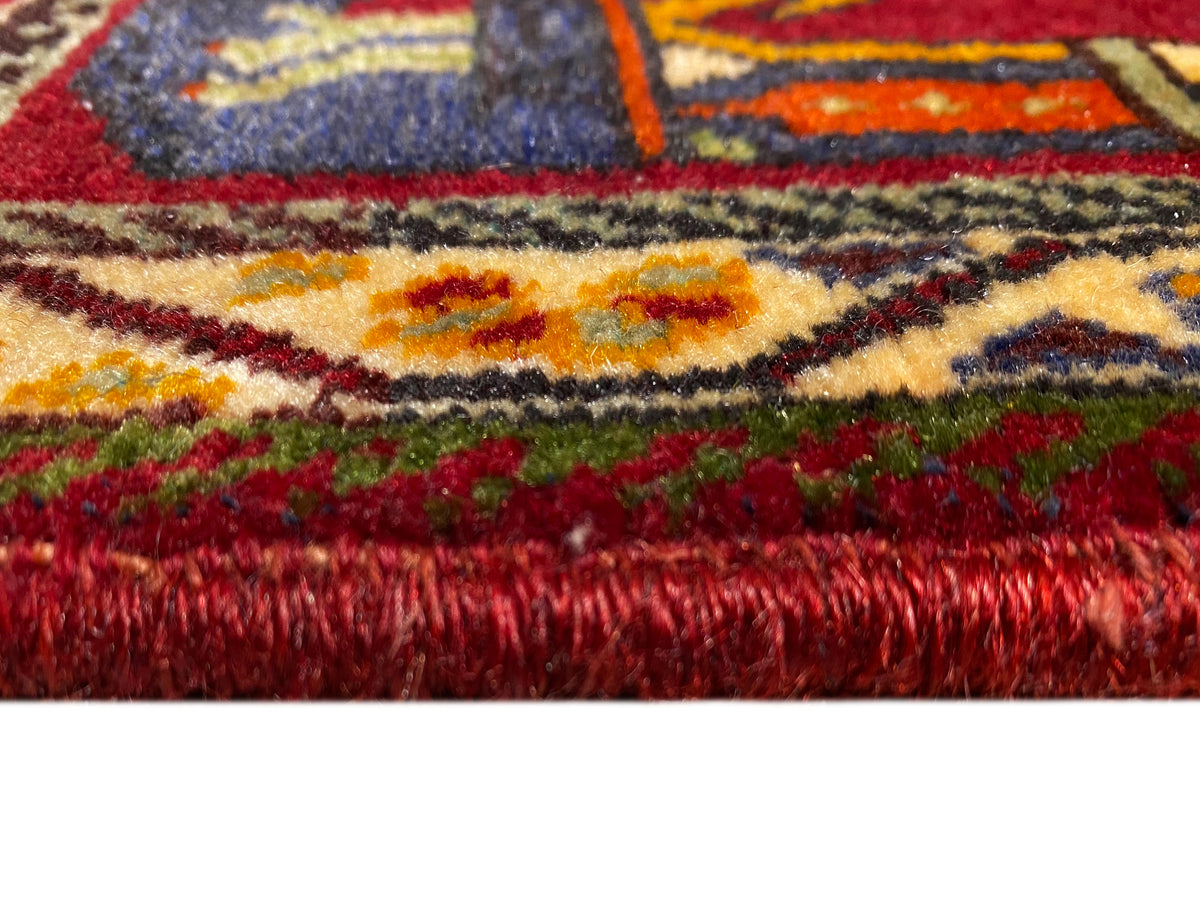 Primo piano del tappeto Poshti (59×61 cm): vello rosso e bordi variopinti con frange