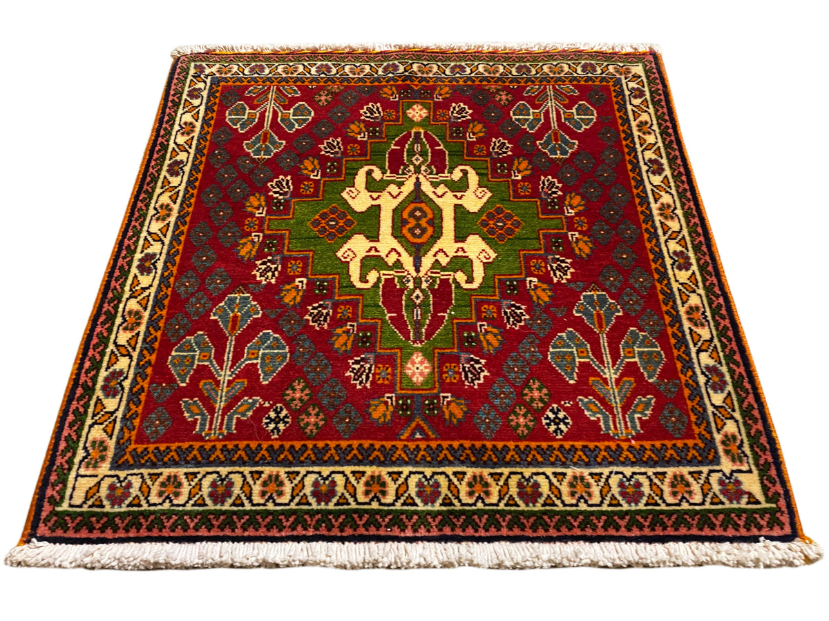 Tappeto orientale con motivo centrale rosso, dettagli verdi e bordo beige, con frange