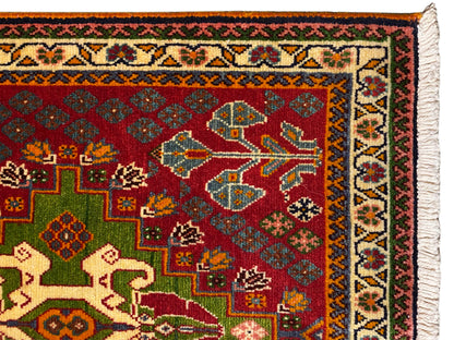 Primo piano: tappeto orientale con fondo rosso, quadrati verdi, bordo decorato e frange