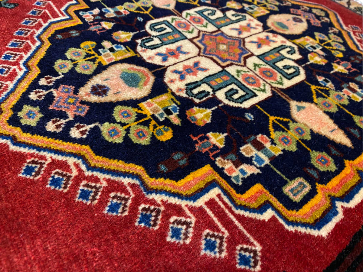 Tappeto Poshti con centro blu scuro, bordi rossi e motivi geometrici variopinti