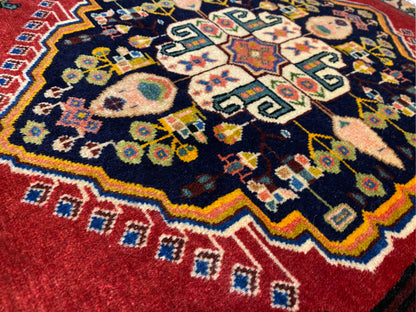 Tappeto Poshti con centro blu scuro, bordi rossi e motivi geometrici variopinti