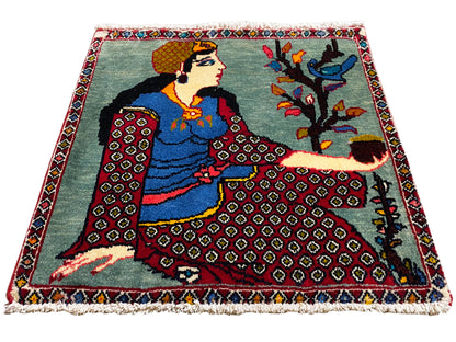 Tappeto Poshti 68x63 cm in vista a tre quarti con figura, albero, bordi decorati rossi, frange