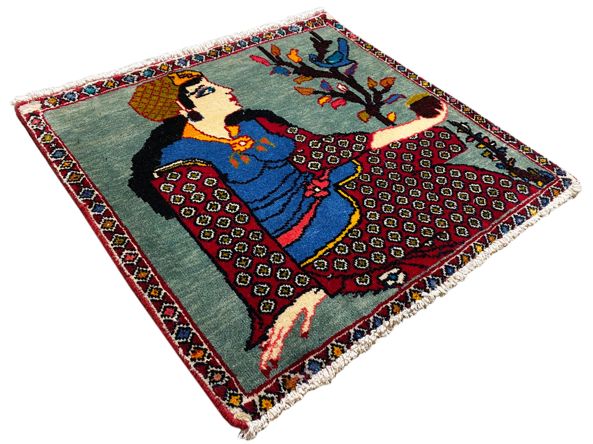 Tappeto Poshti 68x63 cm visto obliquamente dall’alto: motivo figurativo con albero, bordo colorato, frange