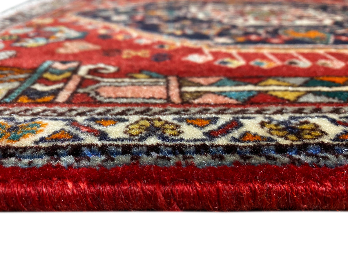 Bordo del tappeto in dettaglio: pelo rosso, bordura decorativa multicolore e frange sfilacciate