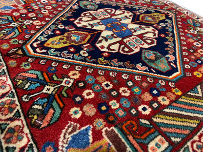 Dettaglio del tappeto: rombi colorati e motivi floreali su sfondo rosso