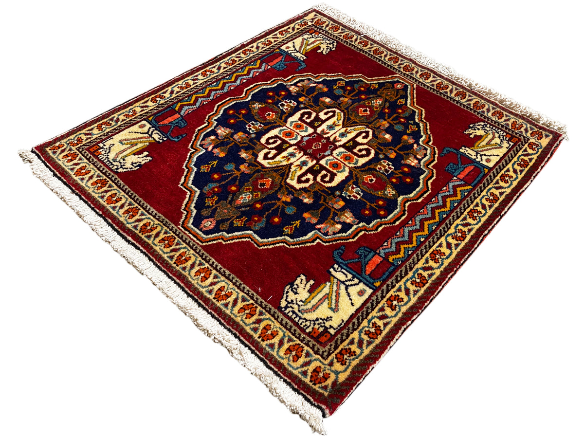 Tappeto con fondo rosso, motivo centrale blu scuro, bordi ornamentali beige e frange