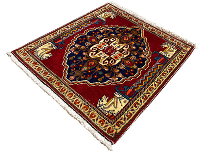 Tappeto con fondo rosso, motivo centrale blu scuro, bordi ornamentali beige e frange