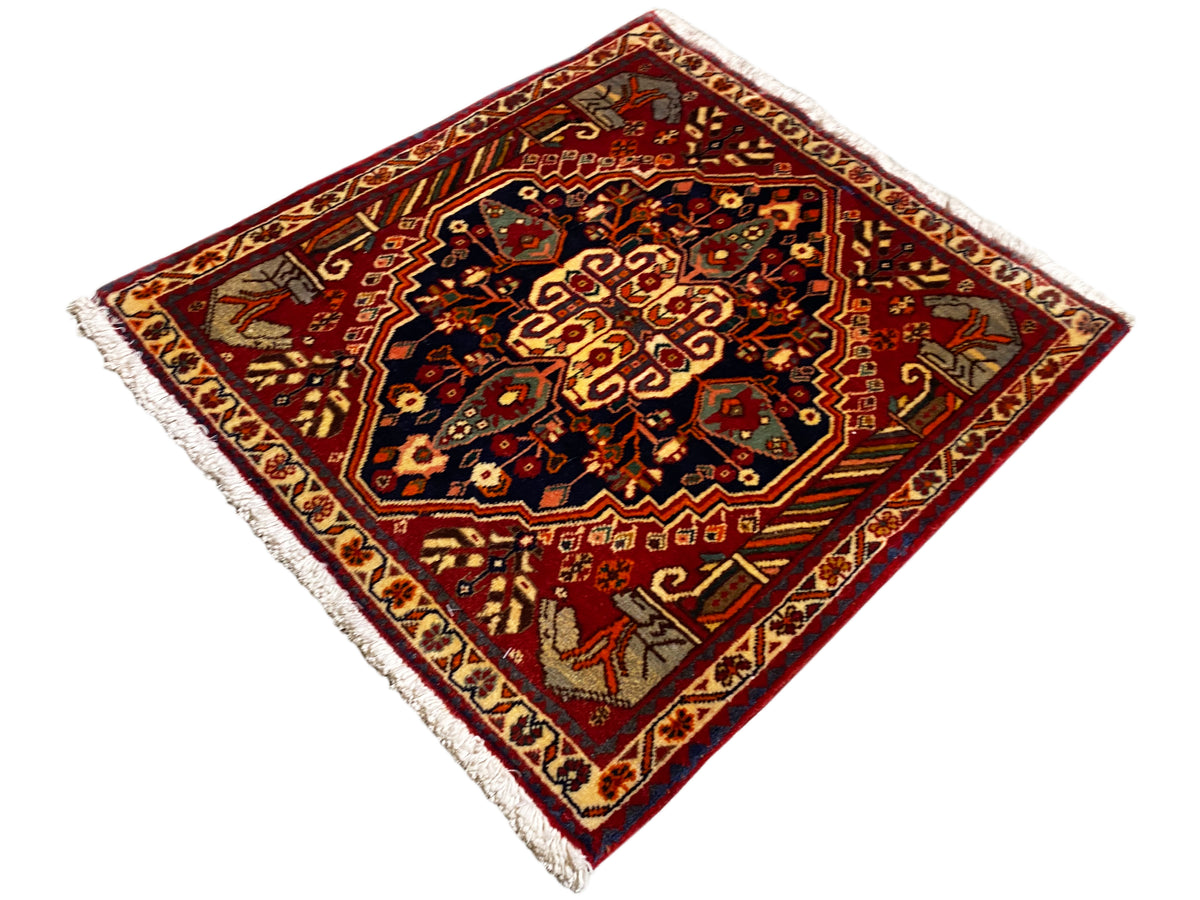 Tappeto 65x59 cm con sfondo rosso, ornamenti centrali scuri e frange sui bordi