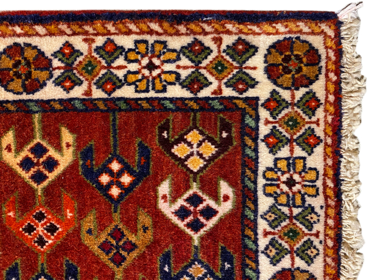 Dettaglio del tappeto: area rossa con bordo ornamentale, rombi colorati e bordi laterali sfrangiati