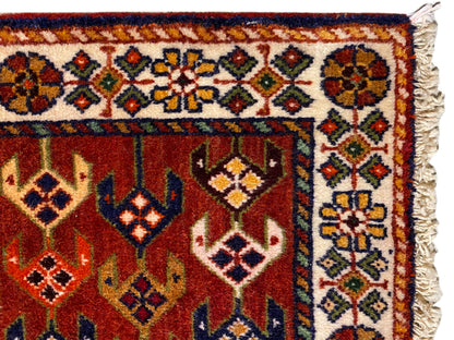 Dettaglio del tappeto: area rossa con bordo ornamentale, rombi colorati e bordi laterali sfrangiati