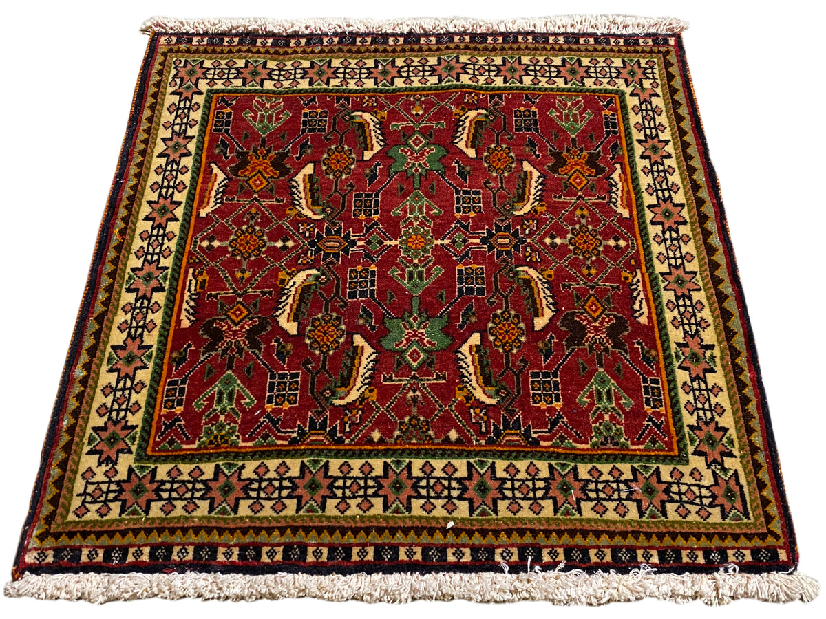 Tappeto Poshti 63x61 cm, vista obliqua: motivo ornamentale rosso su fondo verde e beige.