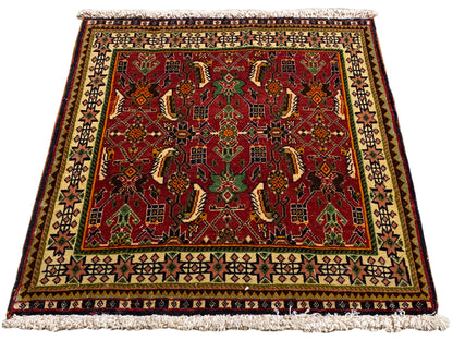 Tappeto Poshti 63x61 cm, vista obliqua: motivo ornamentale rosso su fondo verde e beige.