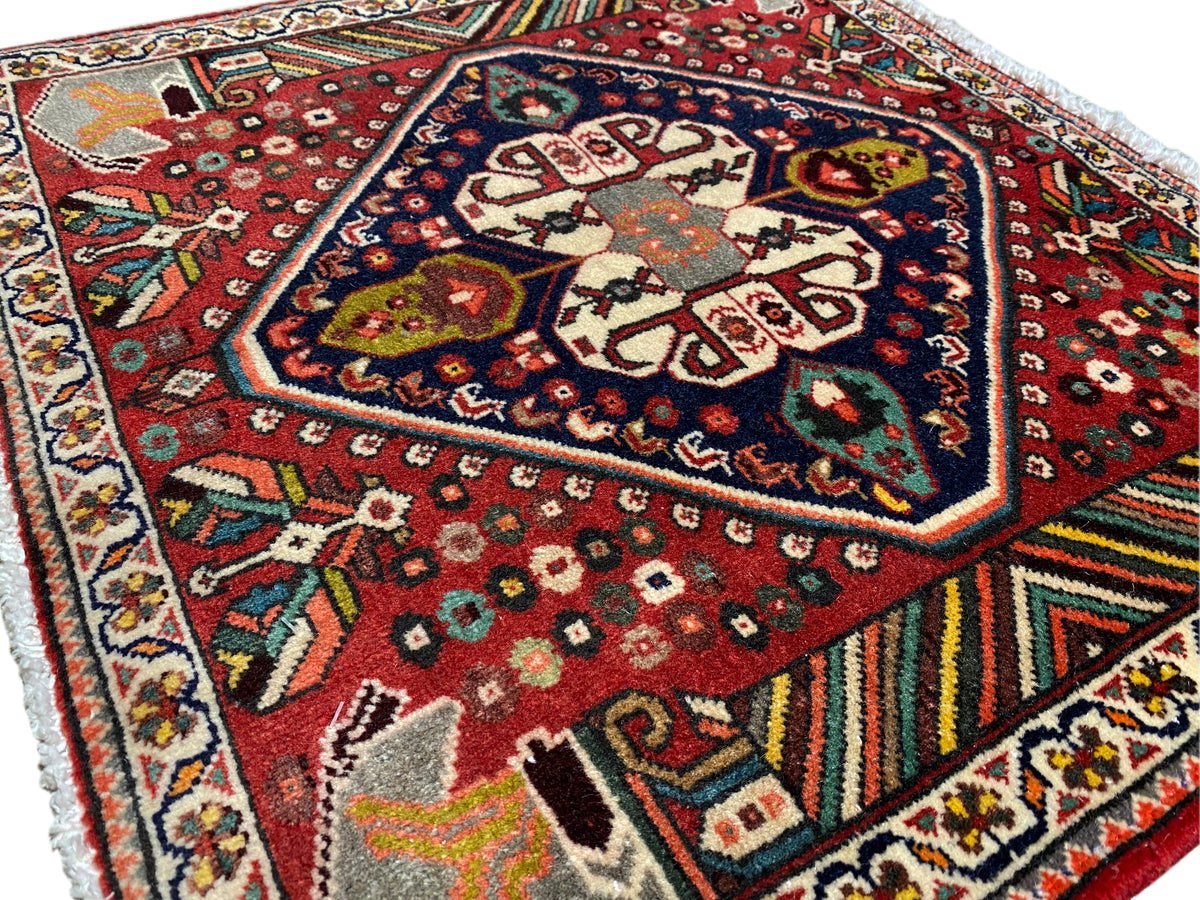 Tappeto orientale fotografato di sbieco: motivo rosso, medaglione scuro e bordature multicolori
