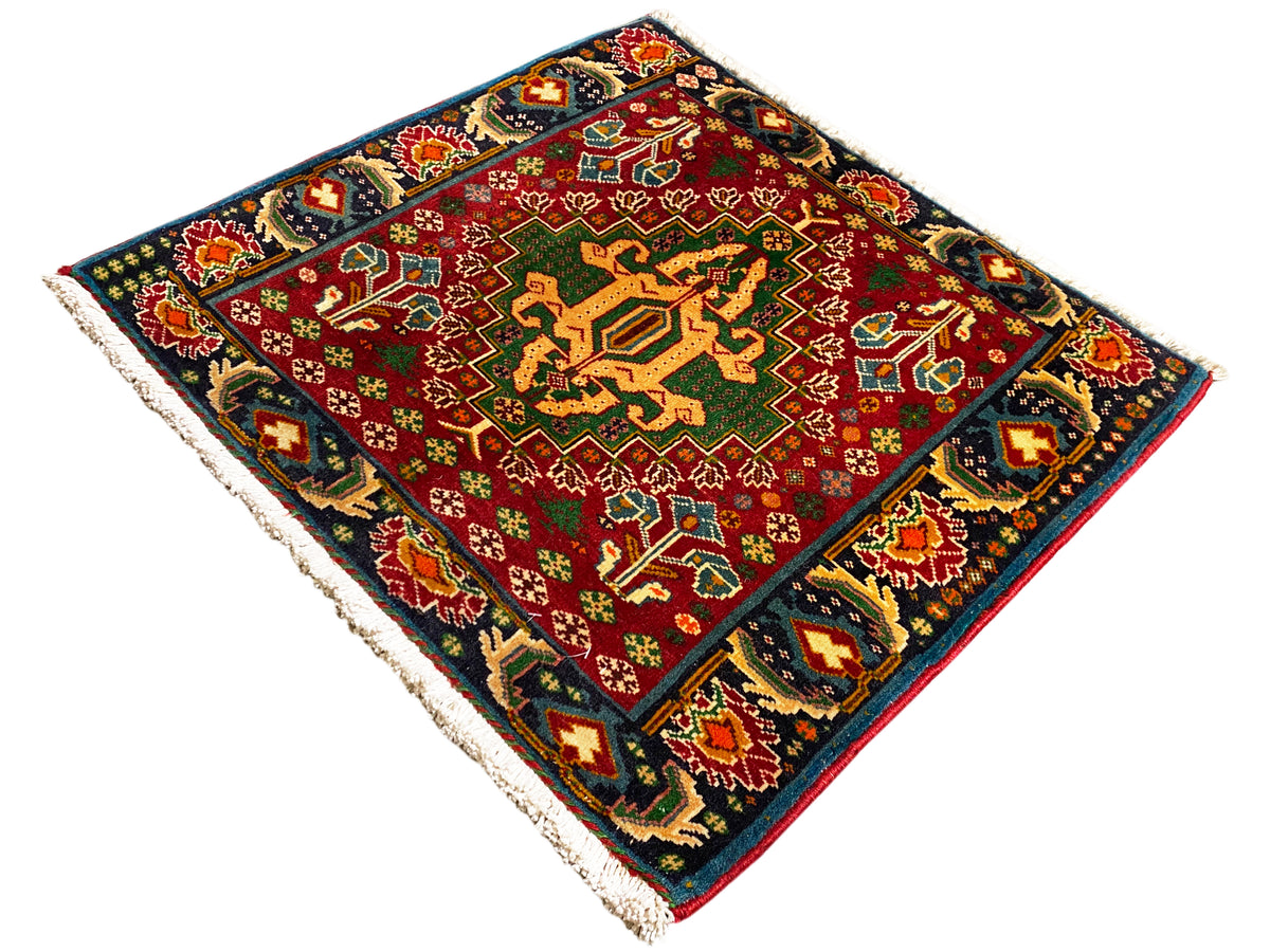 Tappeto rettangolare (67x66 cm) con centro rosso, bordo scuro e ornamenti multicolori, frange