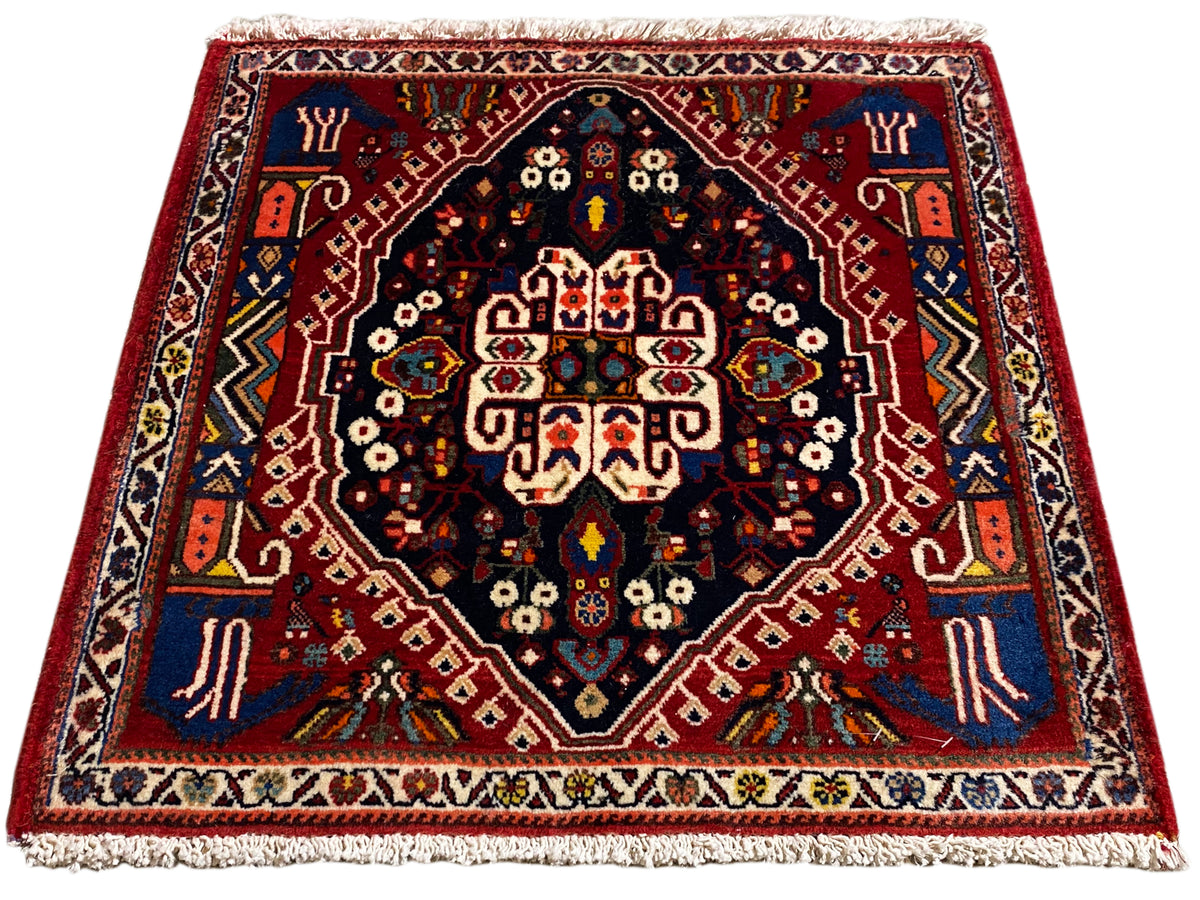 Tappeto con bordo rosso, centro blu scuro e ornamenti multicolori, frange