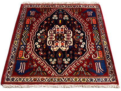 Tappeto con bordo rosso, centro blu scuro e ornamenti multicolori, frange