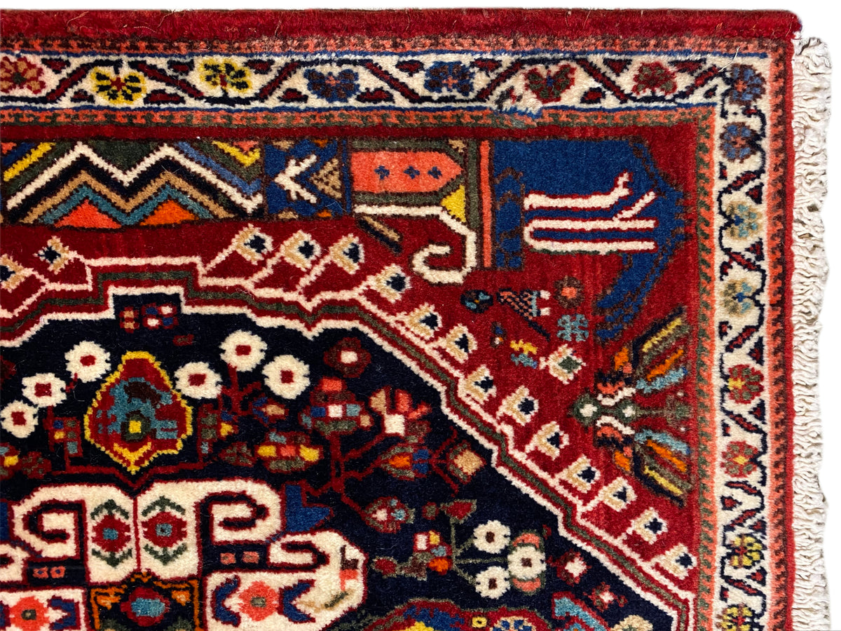 Vista dettagliata del tappeto: sfondo rosso, campo blu scuro, ornamenti e bordura