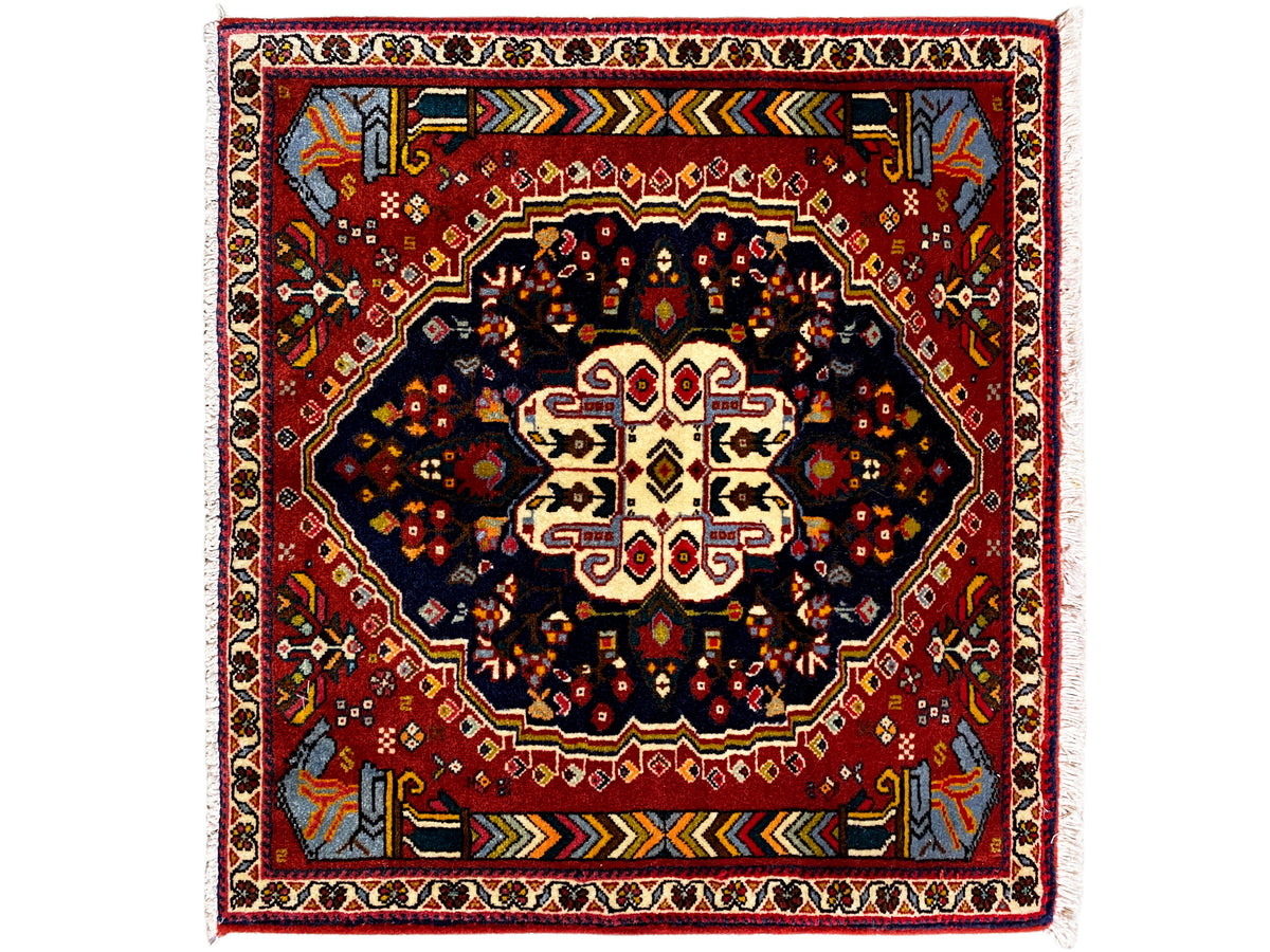 Tappeto Poshti 65x61 cm con bordo rosso, motivo centrale scuro e ornamenti colorati